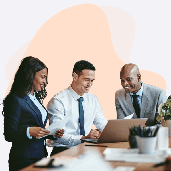 Three IT professionals in formal attire collaborating around a laptop, reviewing documents, and discussing managed IT support solutions in a modern office environment