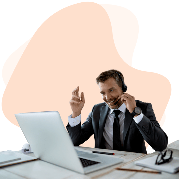 A professional man in a suit wearing a headset, engaged in a conversation while working on a laptop, providing IT support for a small business.