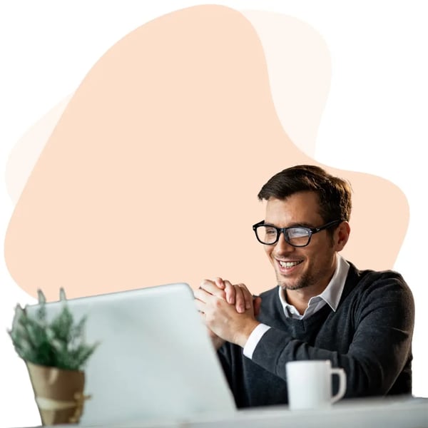 Smiling professional man on a video call with a laptop, coffee mug, and plant in a home office environment.