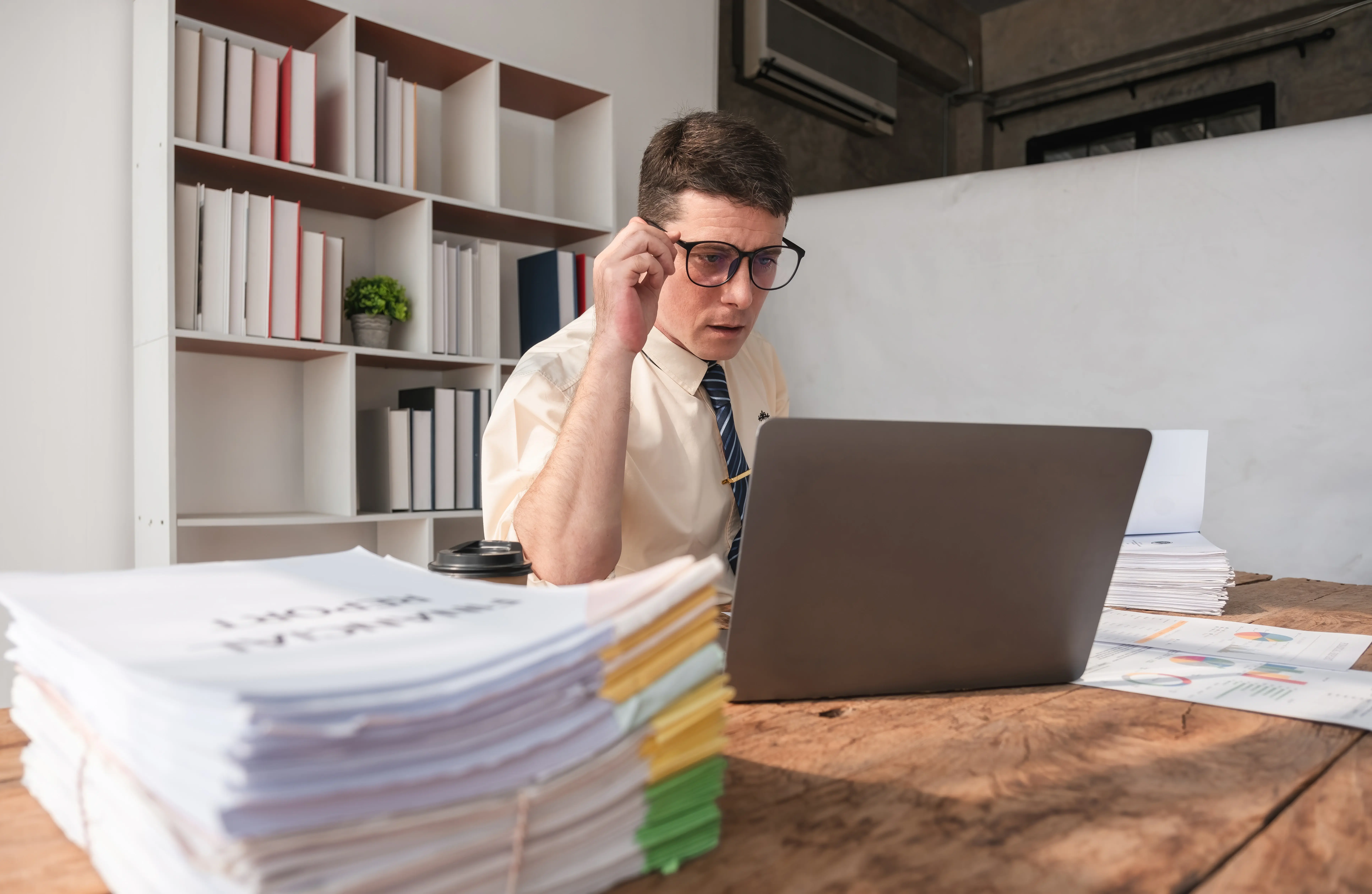 AI automation for small business: office manager working through a stack of paperwork at a laptop