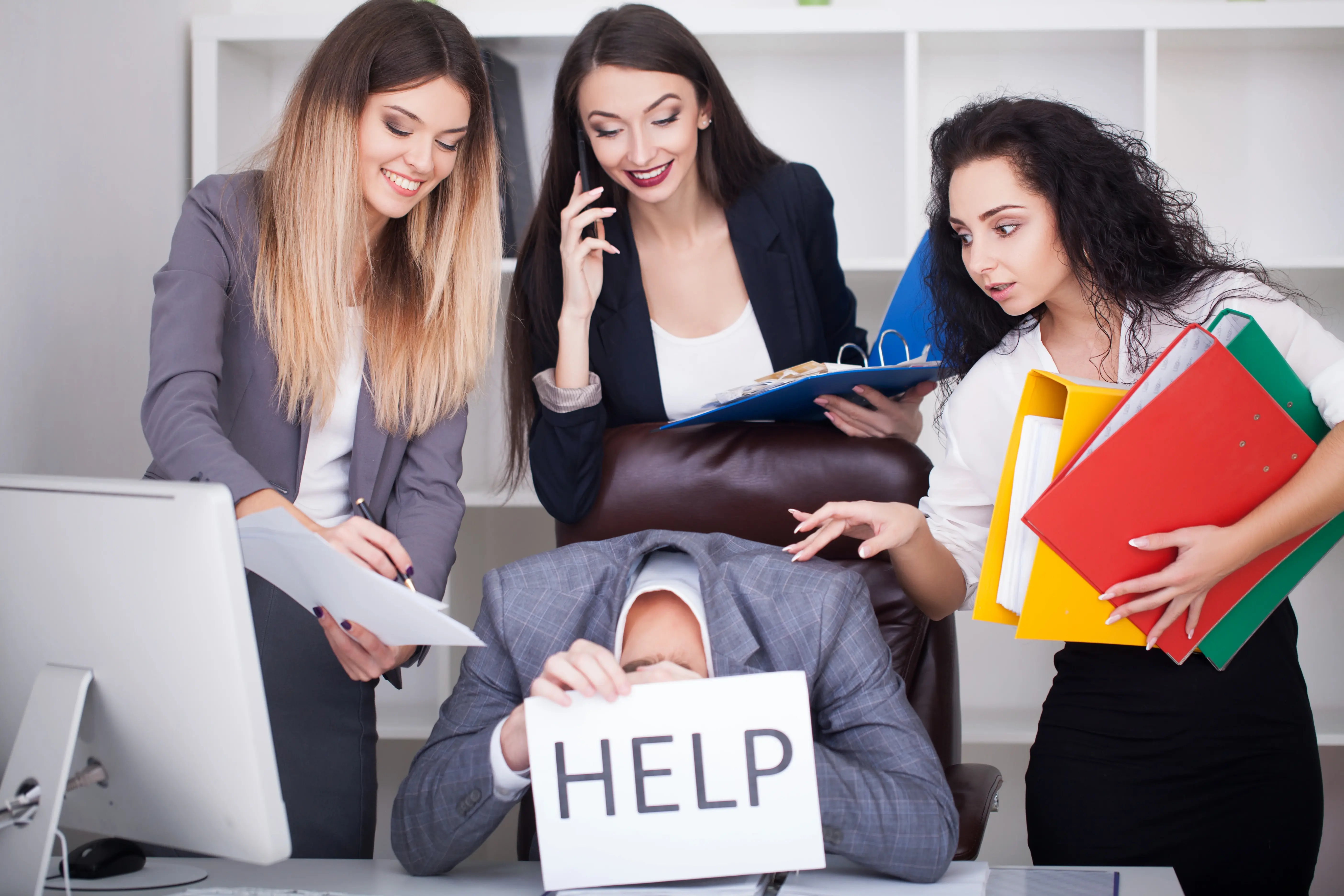 Signs your business needs Managed IT: an overwhelmed business owner holding a HELP sign at his desk while colleagues pile on paperwork.